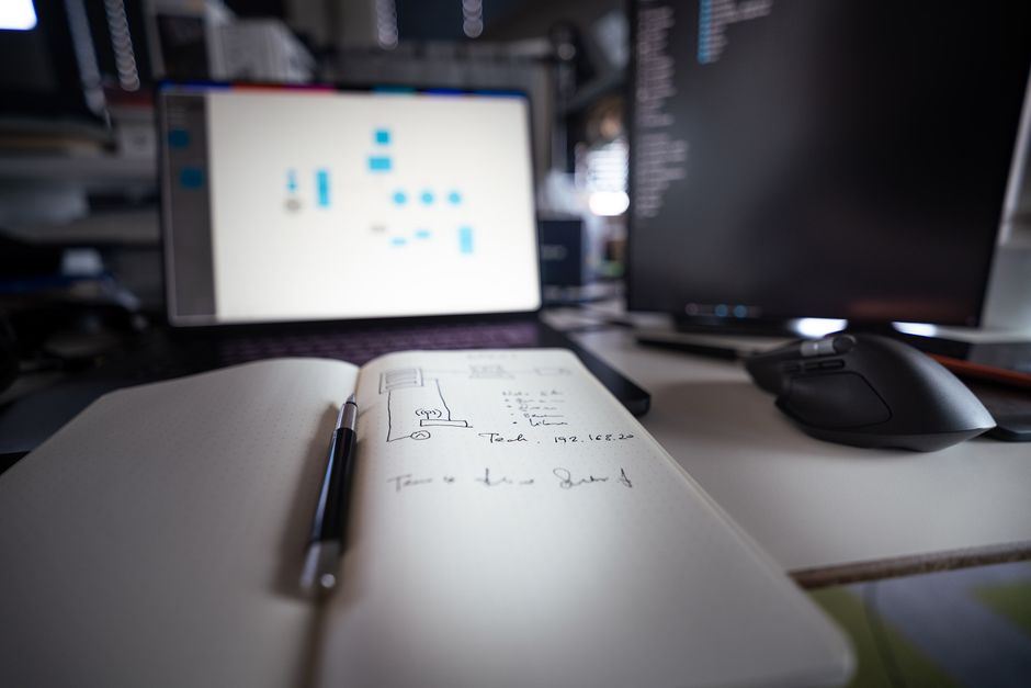 Close-up of a modern desk setup featuring notebooks, monitors, and a computer mouse.